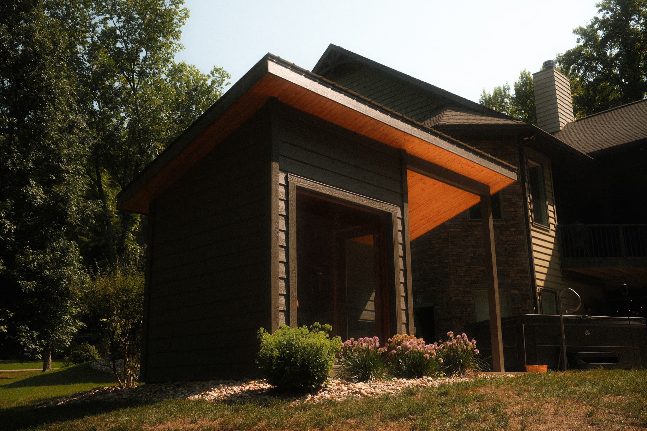 The sauna's roofline angled against the treeline at dusk, warm light spilling from the cedar soffit.